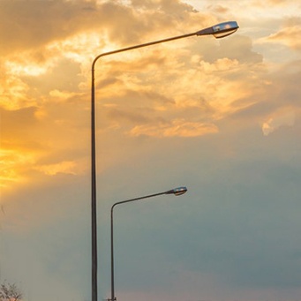 Street light poles with a cloudy sky in the background.